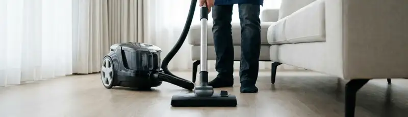 Professional house cleaner vacuuming a living room floor with a canister vacuum cleaner, Oklahoma City, OK.