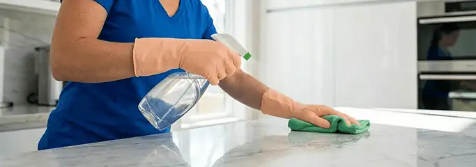 Maid service worker spraying and wiping a kitchen countertop with a microfiber cloth for sanitizing, Oklahoma City, OK.