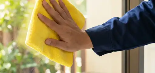 House cleaner wiping a glass window with a yellow microfiber cloth for streak-free cleaning, Oklahoma City, OK.